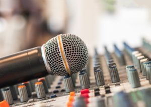 A microphone leans against the knobs on a sound board.