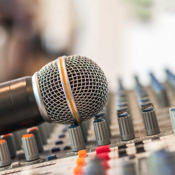 A microphone leans against the knobs on a sound board.