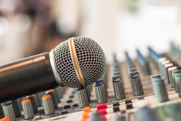 A microphone leans against the knobs on a sound board.