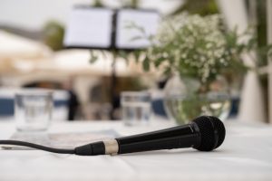 A black microphone sits on a white table cloth, with flowers in the background.