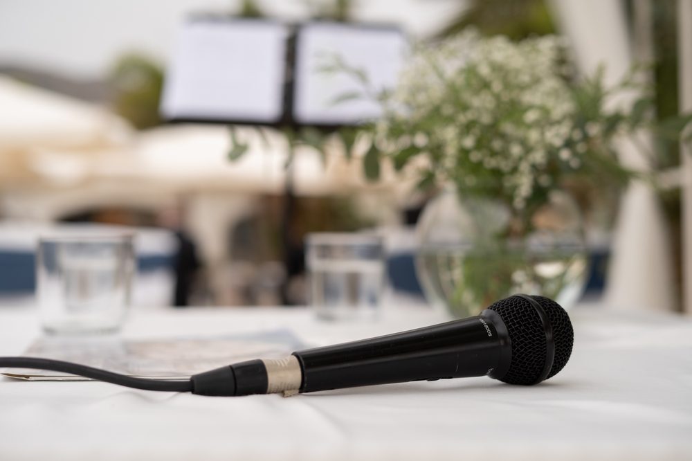 A black microphone sits on a white table cloth, with flowers in the background.