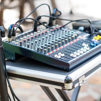 A mixer sits on a table as part of a DJ setup during an outdoor event