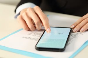 Female hands rest on a smart phone with a digital signature on the screen, with a contract under the phone.