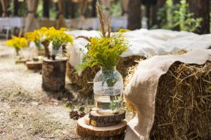 Mason jars of yellow flowers sit at the ends of hay bale seating at a barn wedding.