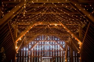 String lights decorate the timbered ceiling of a barn wedding.