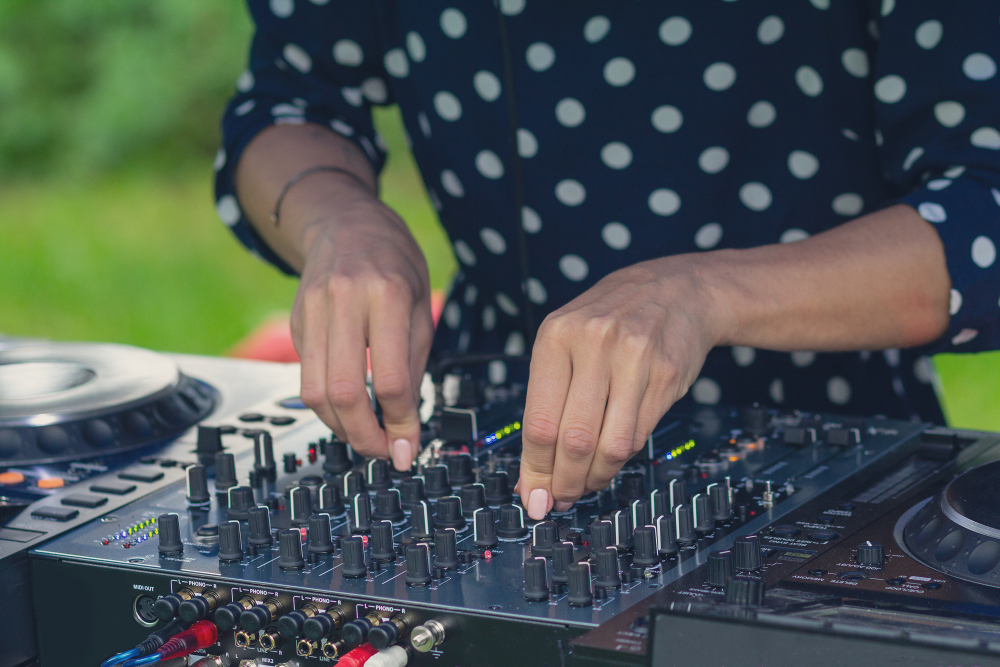 A woman's hands turn knobs on a DJ set up outside with grass in the background