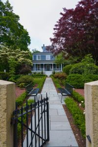 A blue historic house sits at the end of a stone walkway in Cape Cod, MA