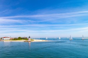 A small lighthouse sits on a sandy beach on a sunny day in Nantucket.
