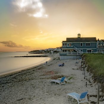 Sun sets over a beach on Cape Cod, with hotels on water in the distance.