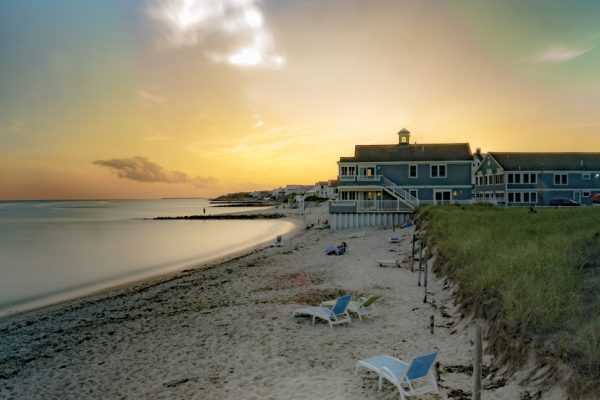 Sun sets over a beach on Cape Cod, with hotels on water in the distance.