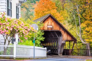 A wooden covered bridge in Vermont with yellow fall foliage behind.