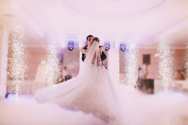 A wedding couple dances in a hall with twinkle lights and a fog effect while a wedding DJ plays music.