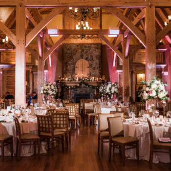A rustic hall with wooden beams filled with tables set for a Maine wedding reception.