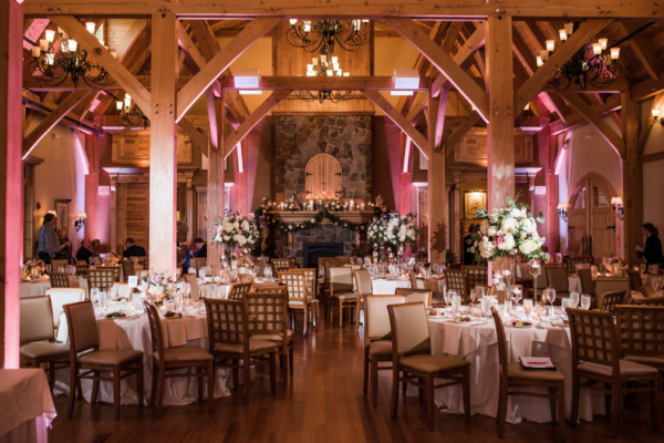 A rustic hall with wooden beams filled with tables set for a Maine wedding reception.