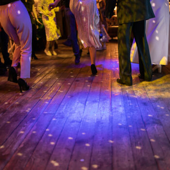 Dancing feet on a wooden floor, lit with party lights during a wedding reception