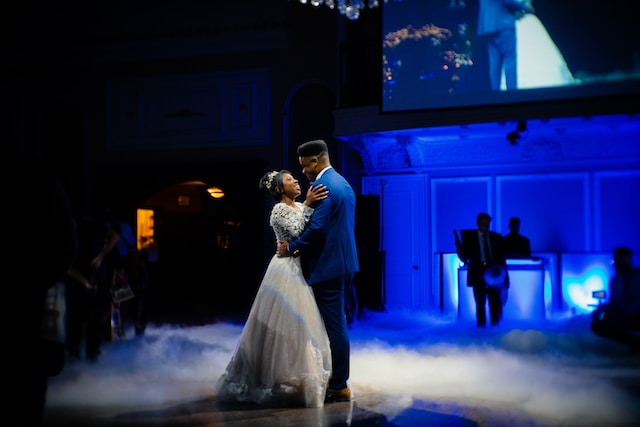 A couple dancing to their first dance song at their wedding against a blue background